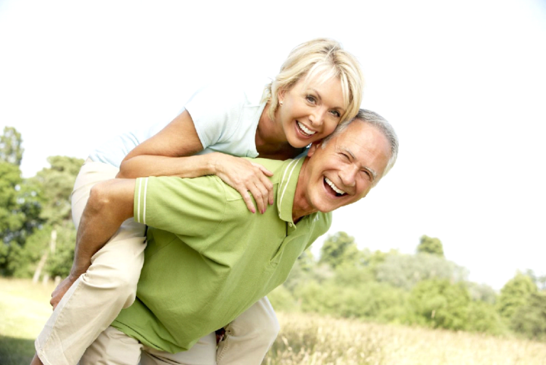 Two people enjoying a sunny day outdoors, with one giving the other a piggyback ride. Their smiles and laughter embody the art of aging gracefully, embracing joy, activity, and vibrant living